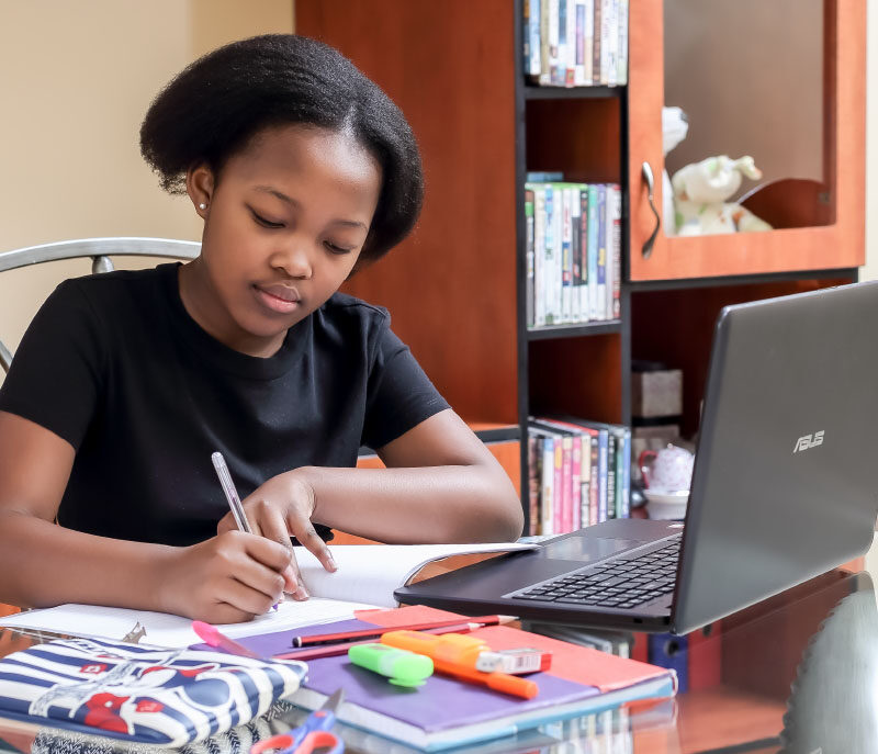 Image of young girl writing in book while using her laptop